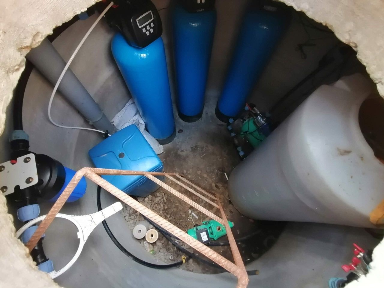 A complete water filtration and softening system installed inside a very tight, underground concrete well pit, demonstrating a challenging installation