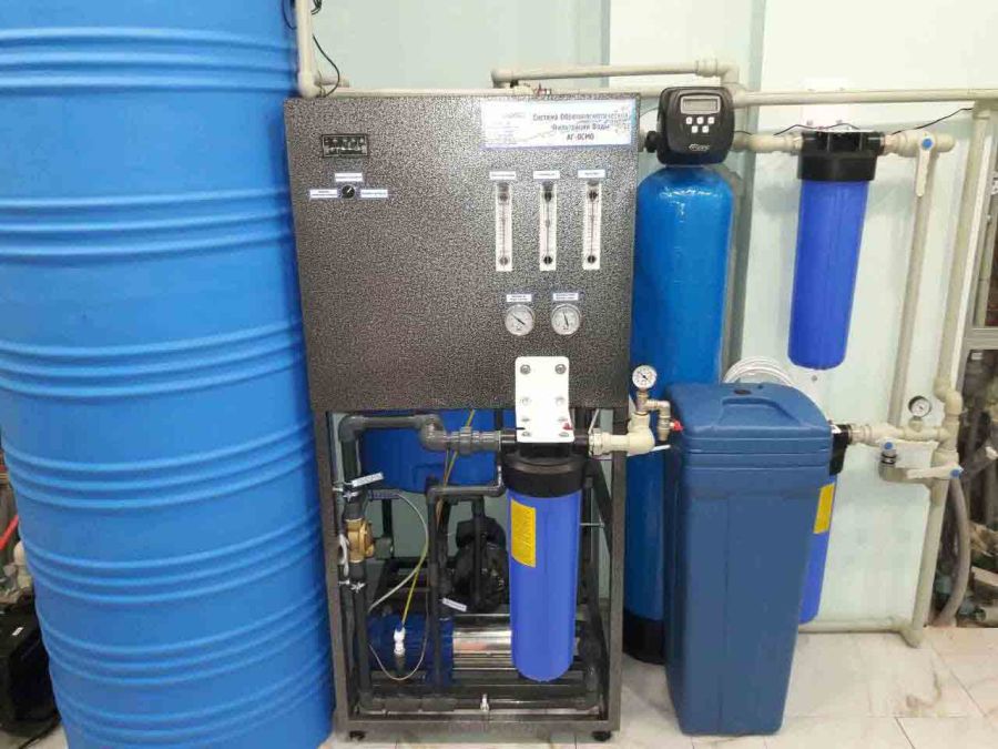 A complete whole-house reverse osmosis (RO) system installed in a utility room, showing the RO unit, large blue water storage tank, and pre-treatment filters