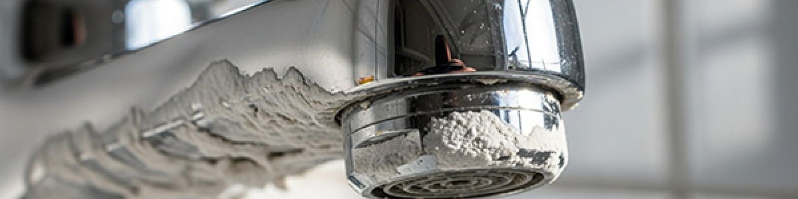 Close-up of a modern chrome faucet clogged with crusty white limescale from hard water