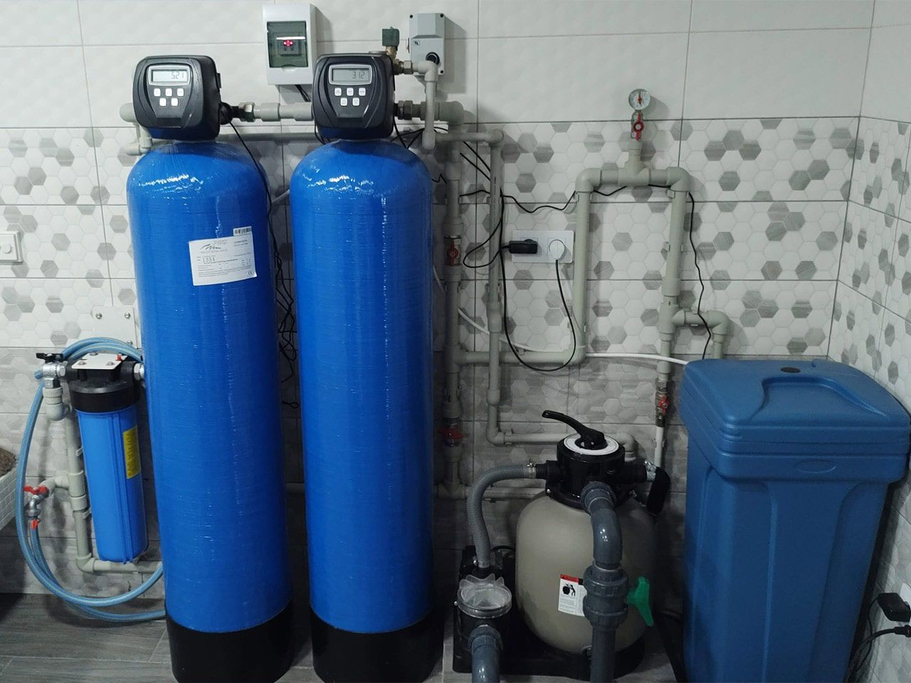 Case study of a multi-tank treatment system for well water, showing dual blue mineral tanks for aeration and softening next to a media filter