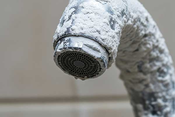 Close-up of a faucet clogged with limescale, a primary sign that answers the question 'what is hard water'.